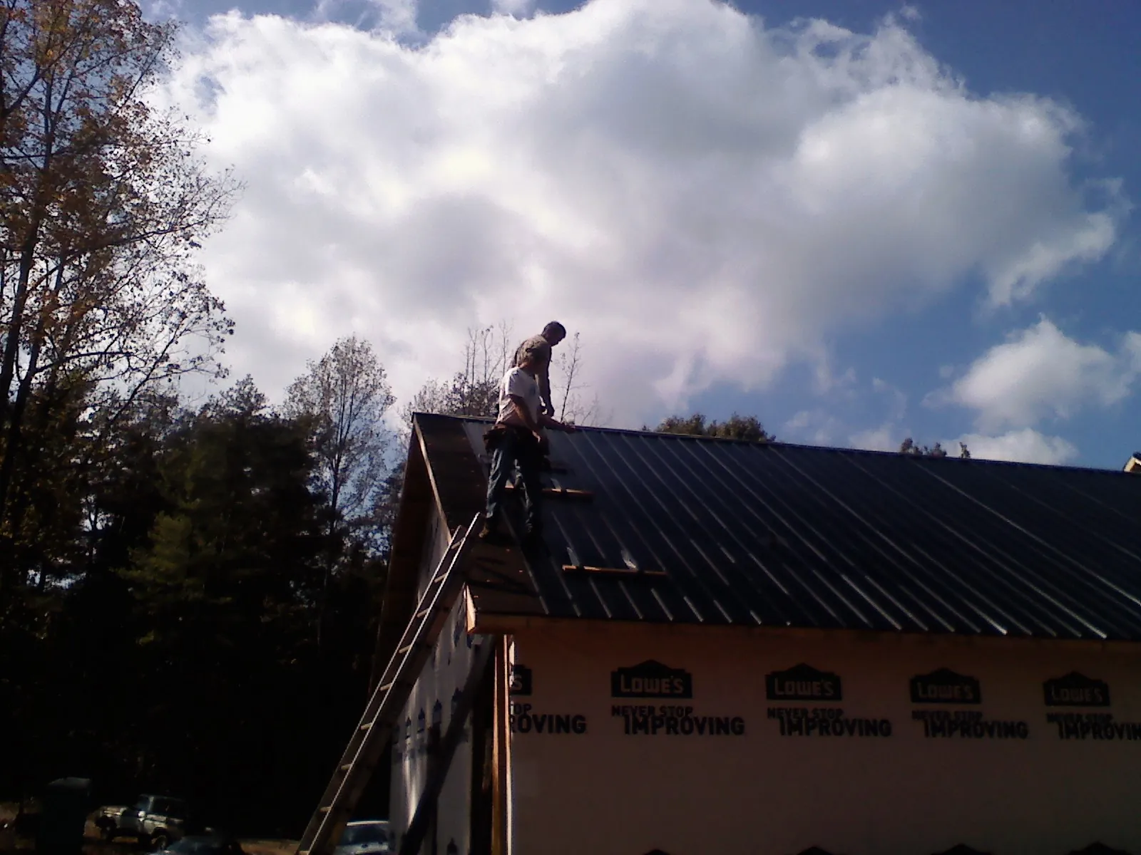 Roofer fastening dark metal panels high against a cloudy sky, from a Roof Inspection job in Bealeton